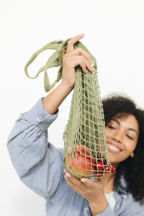 Woman in Blue Long Sleeve Shirt Holding a Net Bag with Fruits