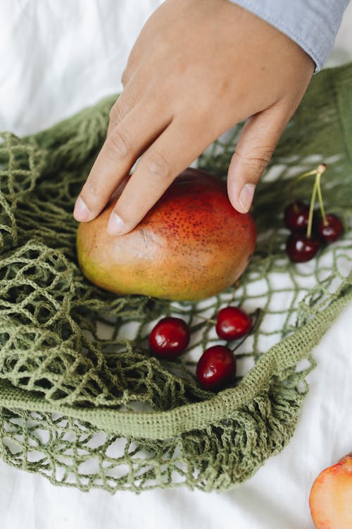 Close-up of a Hand Touching a Mango in a Mesh Bag
