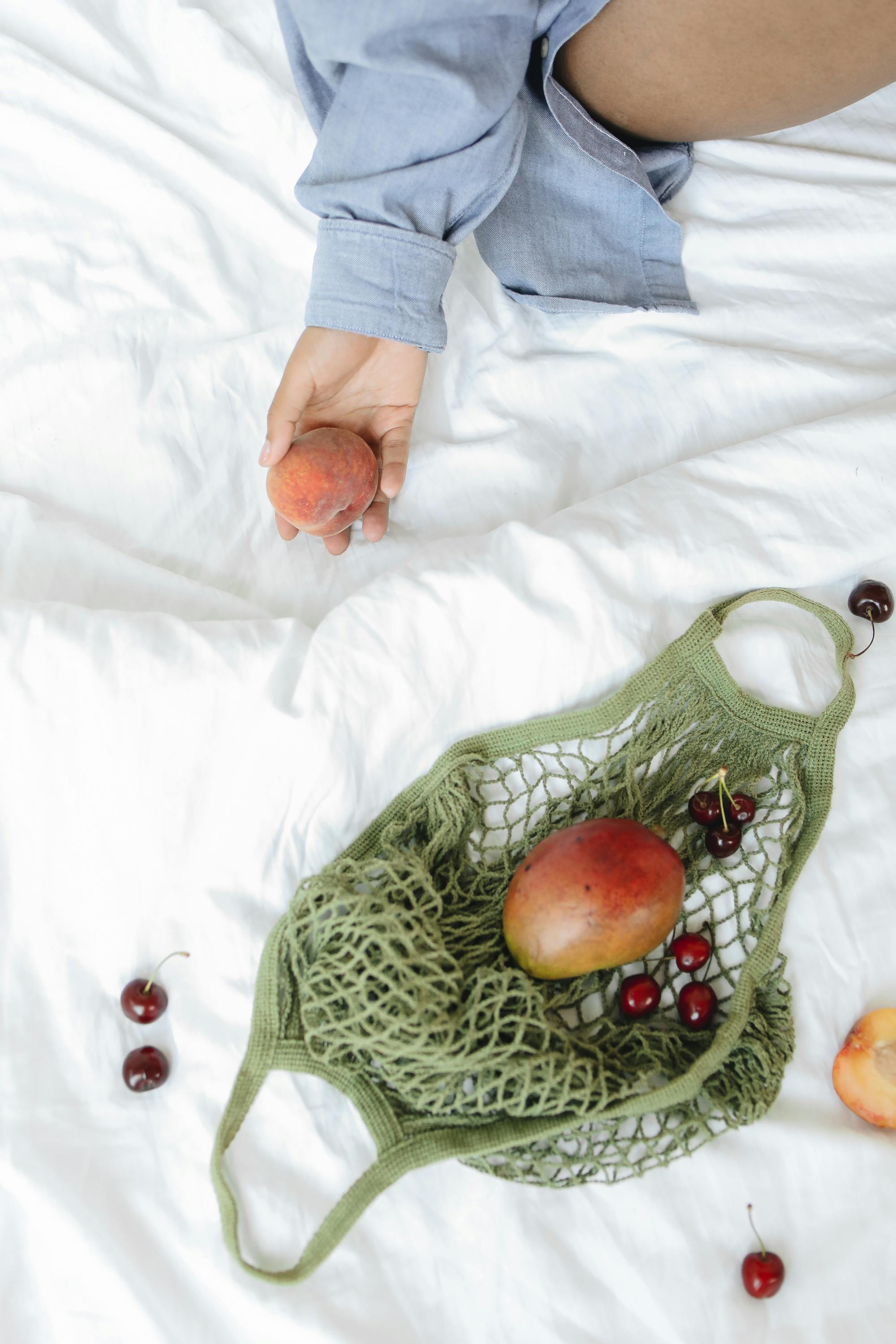 Close-up of hand holding fruit with cherries and mangoes on bed.