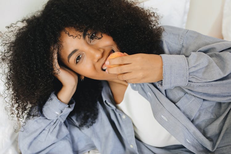 Woman In Blue Long Sleeve Shirt Eating A Round Fruit