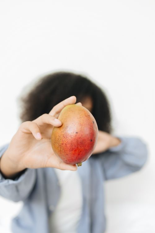 Free A child holding a vibrant mango against a white background, highlighting its vibrant colors. Stock Photo