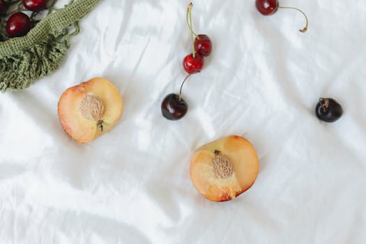 Cherries and peach halves artistically laid on a white fabric background.