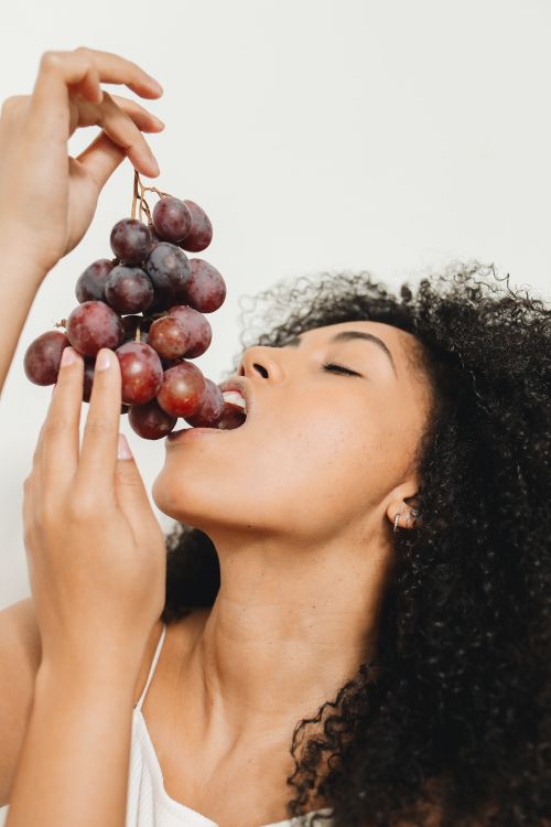Free Close-up of a young woman savoring a bunch of red grapes against a white background. Stock Photo