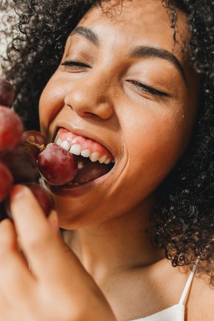 Close-up of a cheerful woman with curly hair enjoying fresh grapes, highlighting healthy eating.