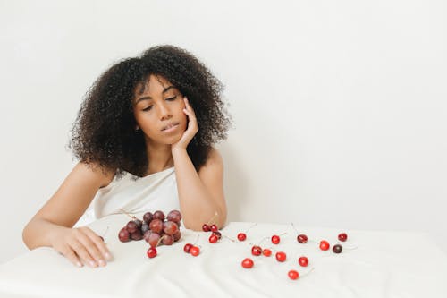 Woman in White Tank Top Sitting Beside the Bed with Fruits