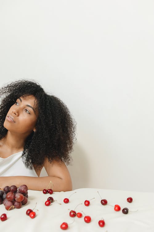 Woman with Curly Hair Sitting by a Table with Fruits