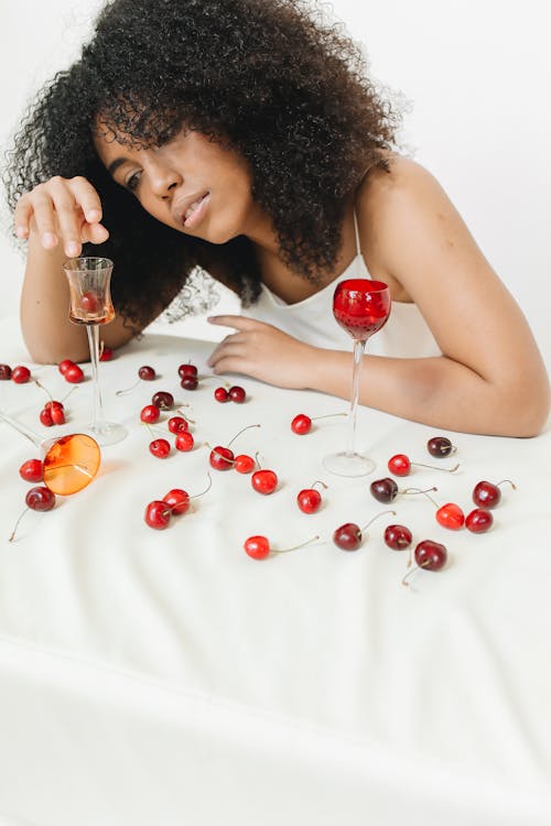 A Woman Sitting by the Table with Cherries and Wine Glasses