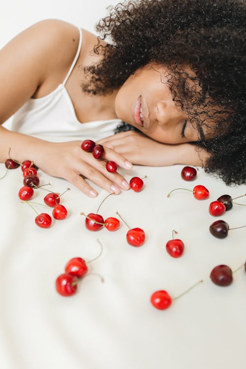Woman Sleeping on White Surface with Scattered Cherries