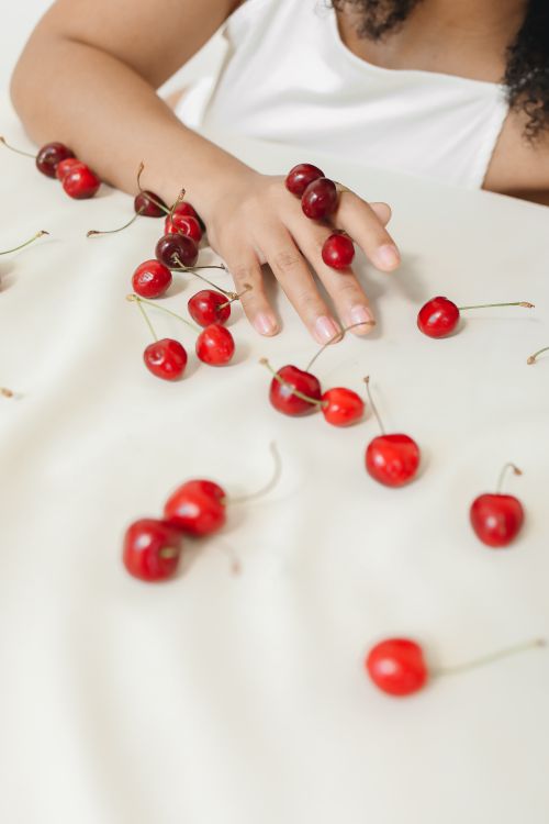 Free A woman's hand gently touching scattered fresh cherries on a soft white surface. Stock Photo