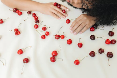 Photo of a Woman with Curly Hair Lying Near Red Cherries 