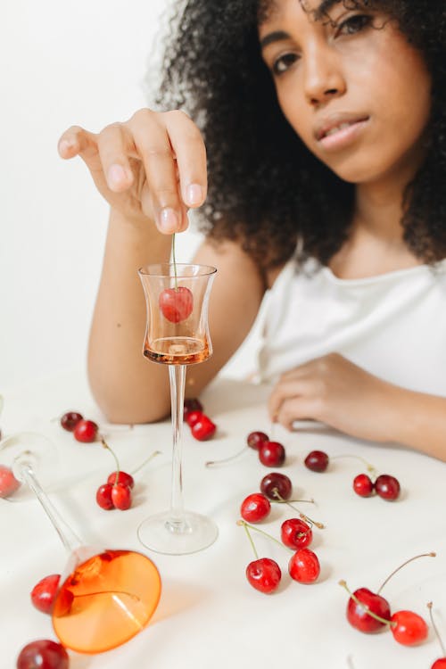 Woman Sitting at the Table and Dipping a Cherry in Liquid in a Glass