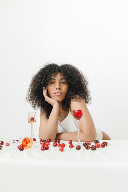 Photo of a Woman with Curly Hair Posing Near Drinking Glasses and Cherries