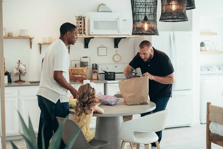 Men Unpacking Groceries At The Table With Their Daughter