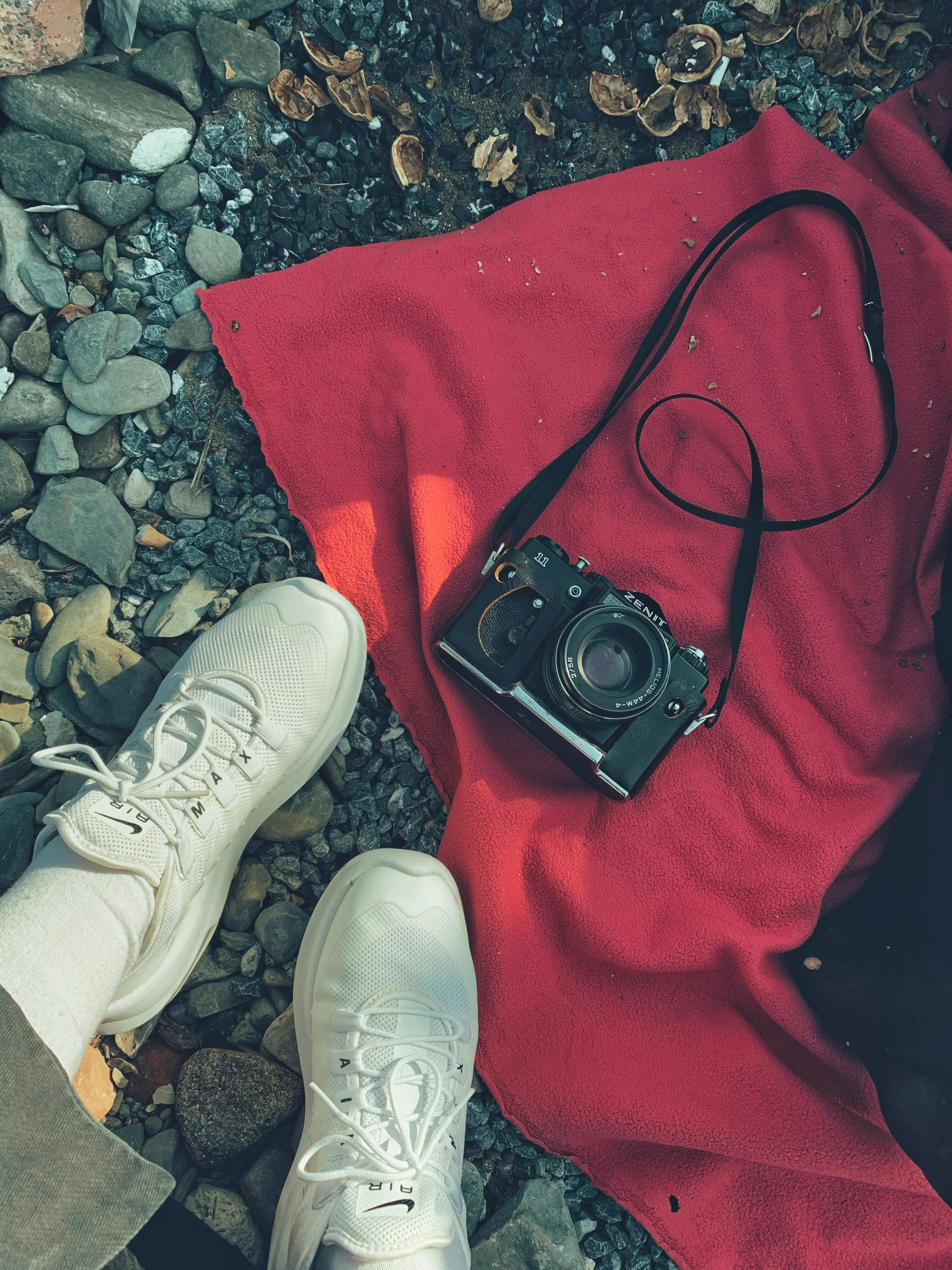 photo of a person s feet in white sneakers near a black camera