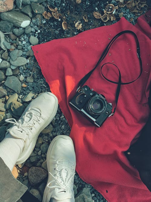Free Photo of a Person's Feet in White Sneakers Near a Black Camera Stock Photo