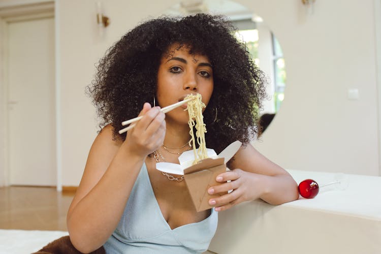 A Woman Eating Noodles In A Takeout Box