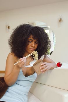 Woman in a blue dress enjoying takeaway noodles at home.
