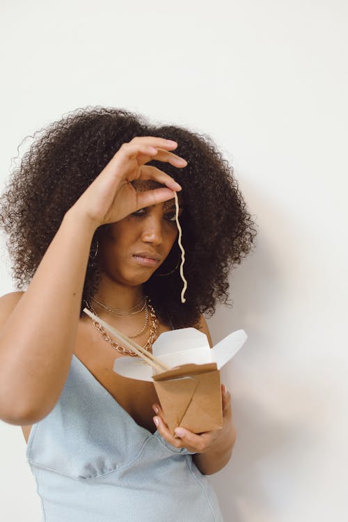 Woman Standing Near White Wall Holding a Noodle