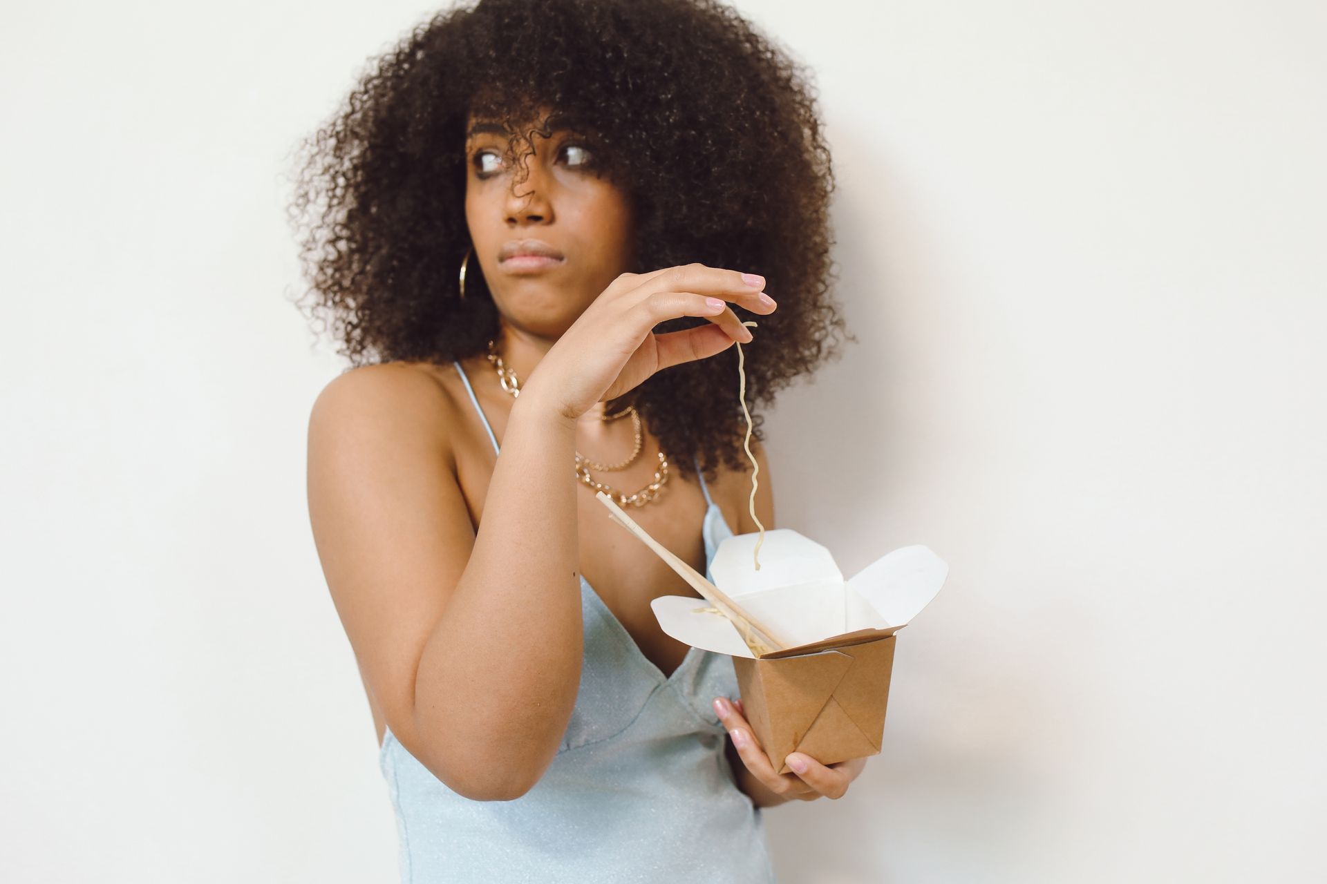 Close-up of a woman with curly hair eating noodles from a takeout box.