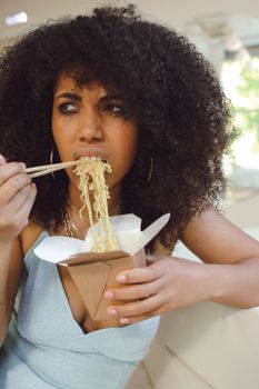 Confident African American woman enjoying noodles with chopsticks indoors.