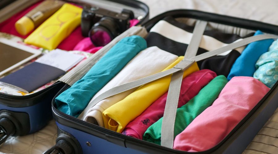 Open suitcase packed with rolled clothes, toiletries and a camera, ready for a trip