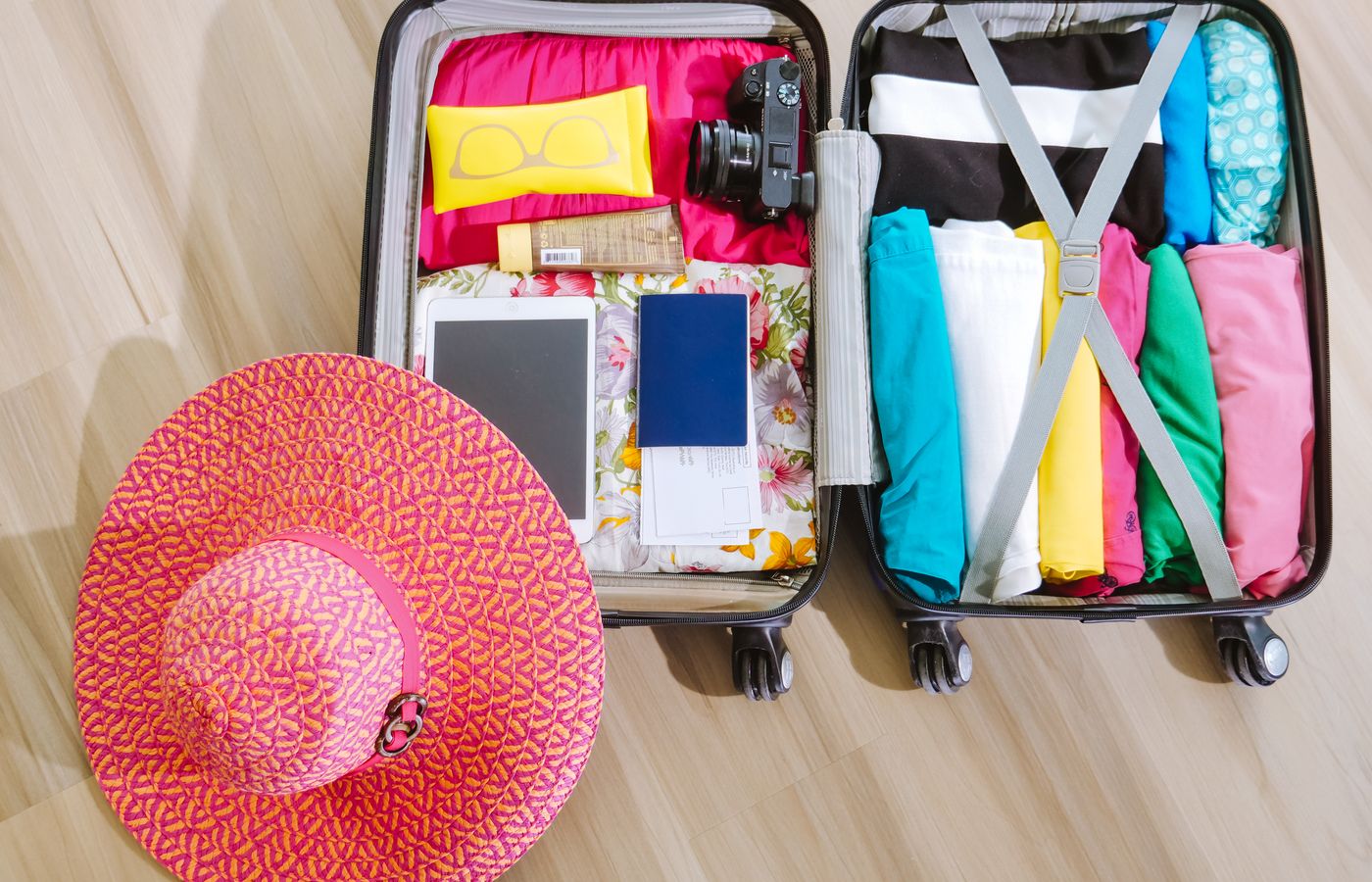 Top view of a suitcase packed with clothes, a camera, and a sun hat, ready for summer travel.