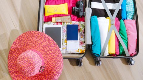 Top view of a suitcase packed with clothes, a camera, and a sun hat, ready for summer travel.