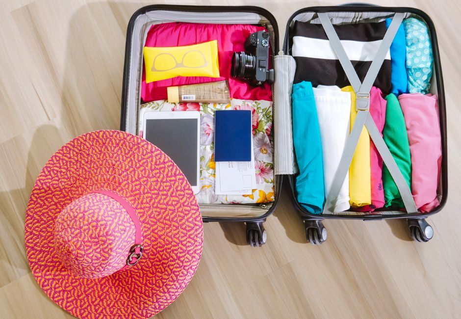 Top view of a suitcase packed with clothes, a camera, and a sun hat, ready for summer travel.