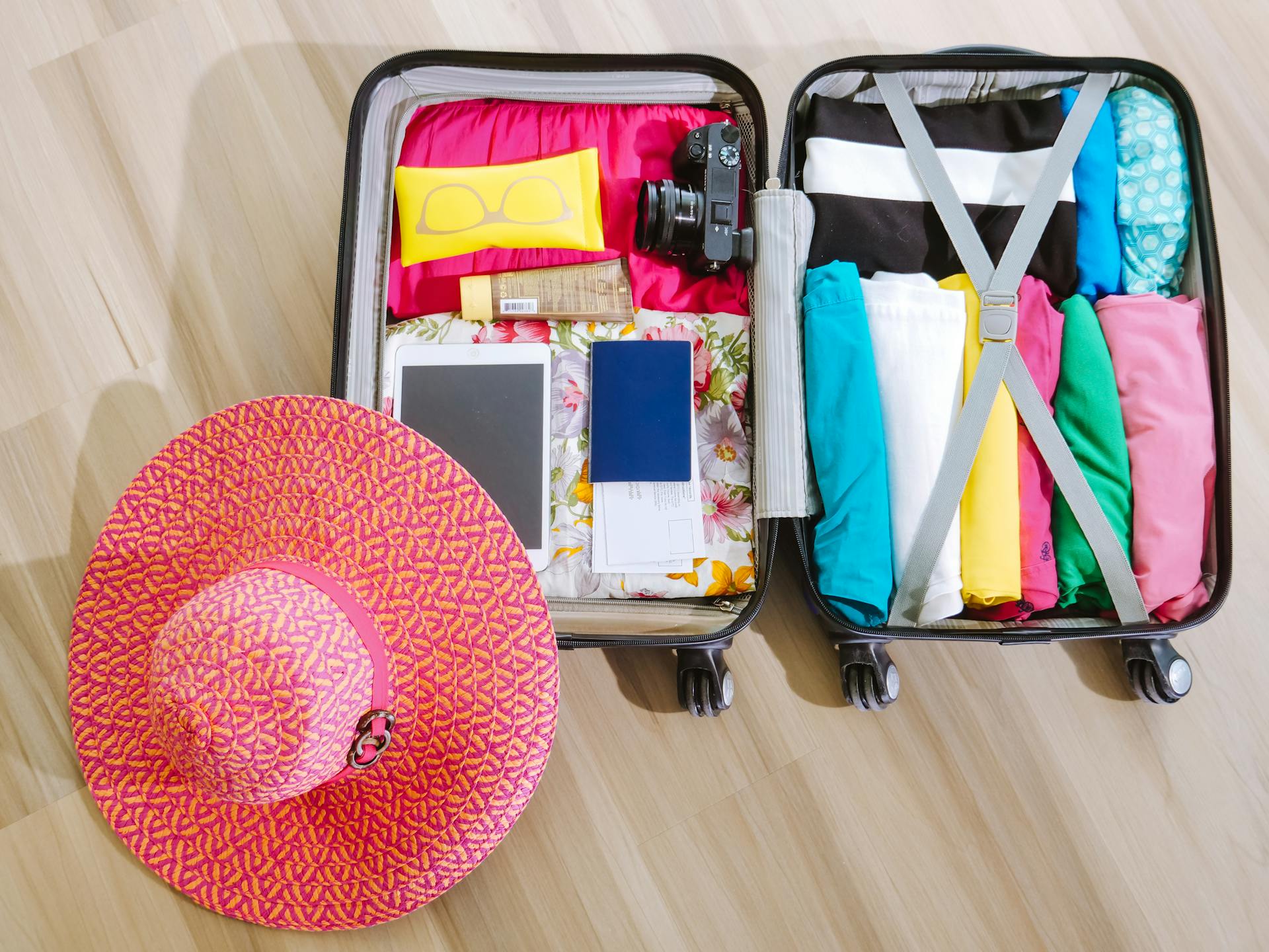 Top view of a suitcase packed with clothes, a camera, and a sun hat, ready for summer travel.