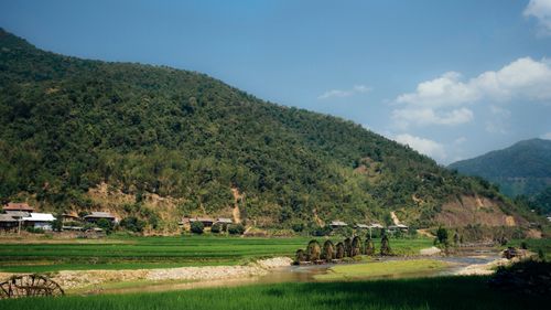Free Picturesque rural landscape with a stream beside lush green mountains and a quaint village. Stock Photo