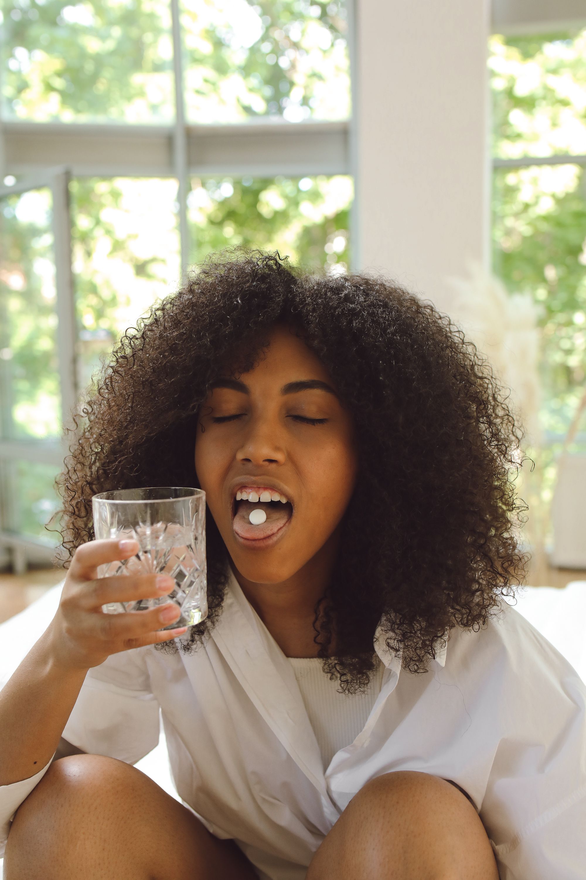 Close-up of a woman with afro hair taking medication indoors.