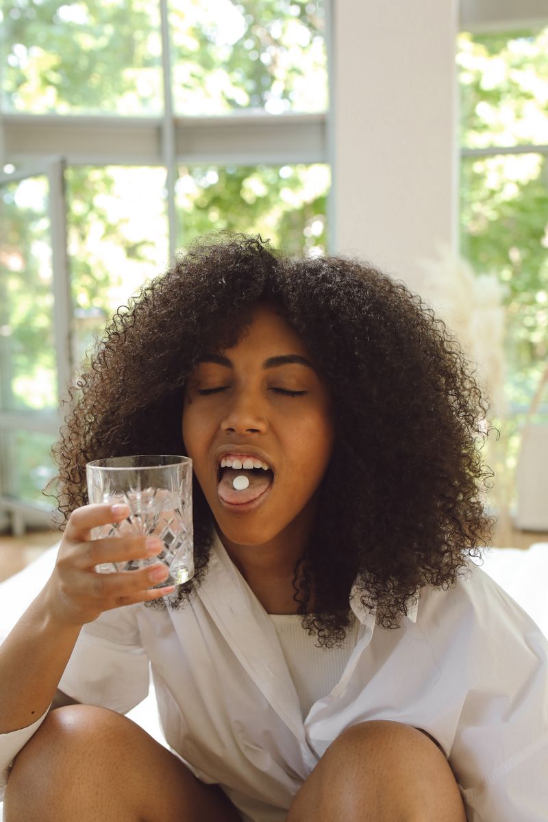 A Black woman with natural hair takes a single pill with a glass of water in a sunlit room, the way a daily PrEP dose fits into an ordinary morning.