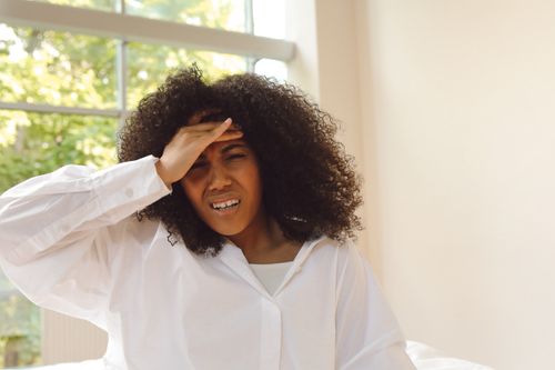 Free African American woman experiencing headache, holding forehead in discomfort indoors. Stock Photo