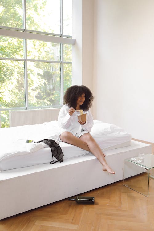 Woman Eating Takeaway Noodles while Sitting on the Bed