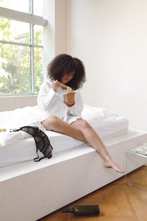 Lazy Woman Sitting on Bed Eating Noodles