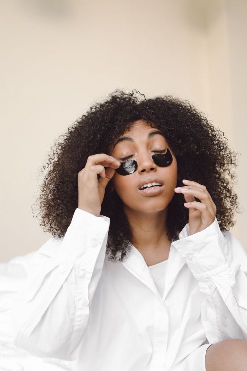 Free African American woman with afro hair applying skincare patches under eyes indoors. Stock Photo