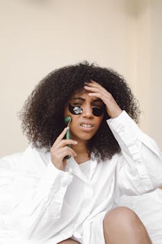 African American woman using a jade roller with under-eye patches for skincare.