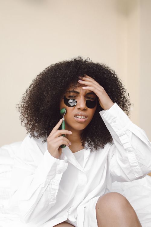 Free African American woman using a jade roller with under-eye patches for skincare. Stock Photo