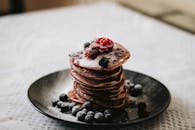 一盘蓬松的煎饼，点缀着新鲜的蓝莓和乌藨子，撒上了糖