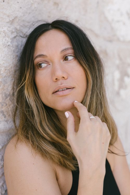 Free Portrait of a woman with natural beauty, leaning against a wall, looking thoughtful. Stock Photo