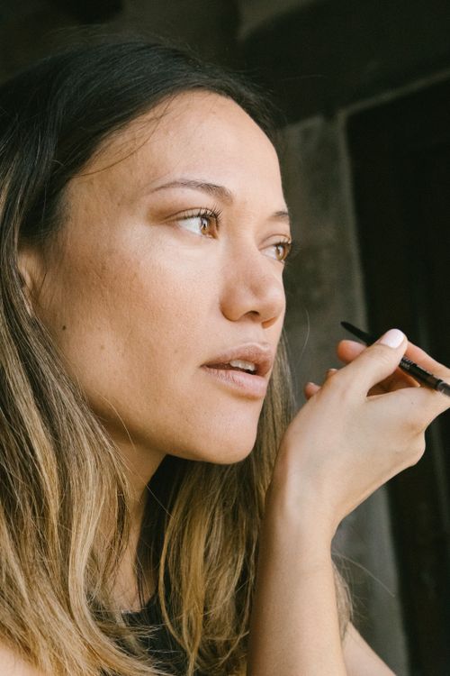 Free Beautiful woman in profile view applying makeup with pencil indoors. Stock Photo