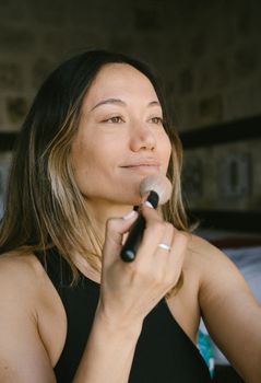 Woman in a black top using a makeup brush indoors, showcasing a beauty routine.