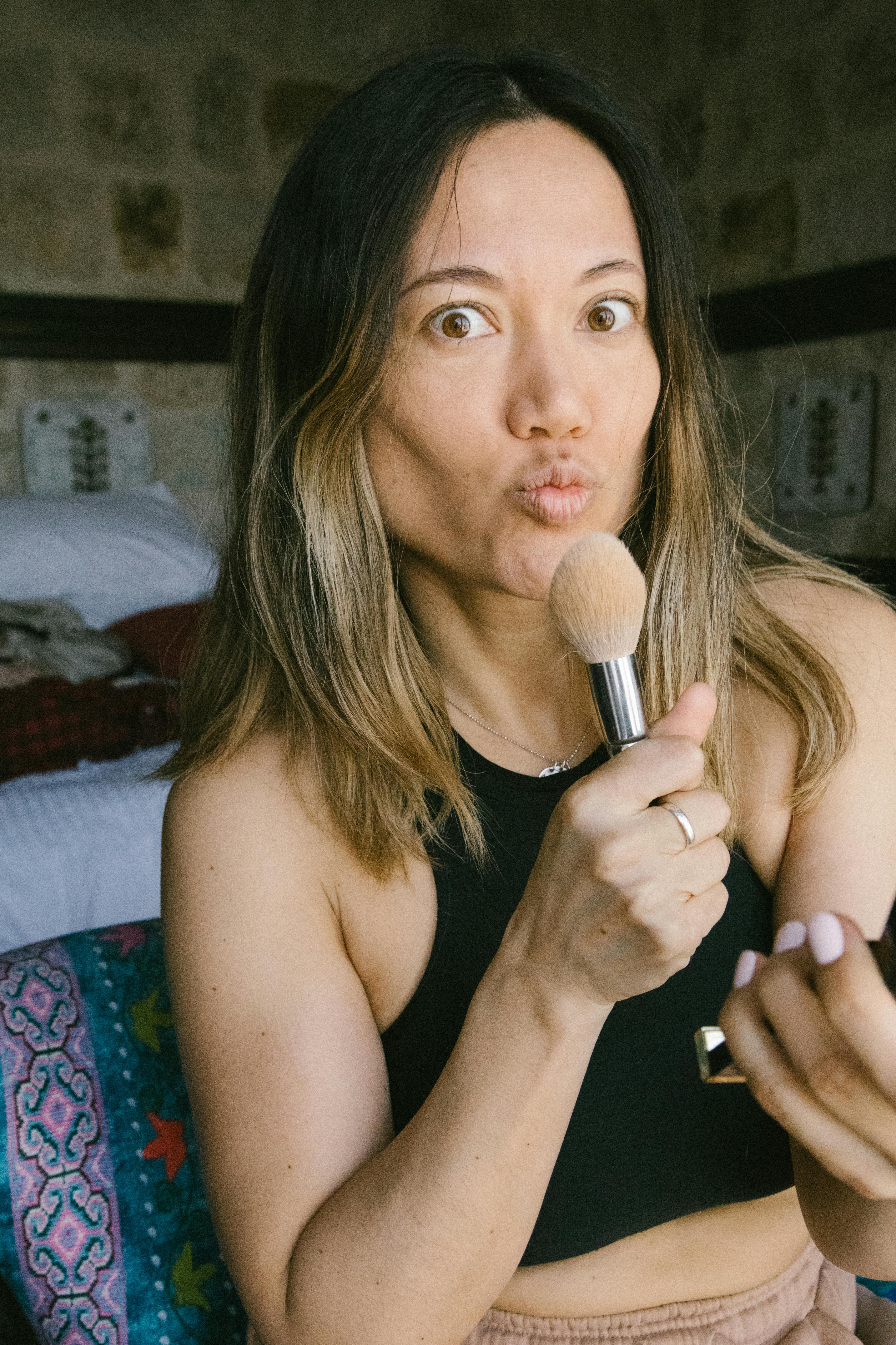 woman making faces while holding makeup brush