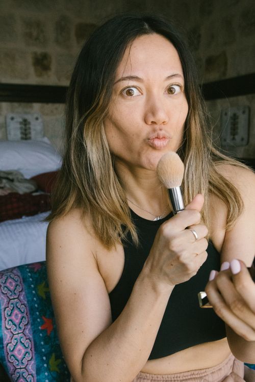 Free A woman in a black top playfully applies makeup with a brush indoors. Stock Photo