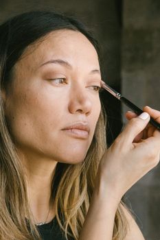 Close-up of a woman applying eyeshadow with a brush indoors, showcasing a natural beauty routine.