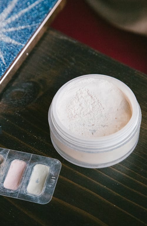 Powder in Round Jar and Eye Shadows on Brown Wooden Table