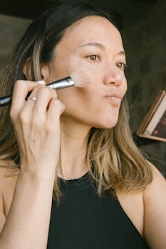 Close-up of a woman applying makeup with a brush indoors, focused on beauty routine.
