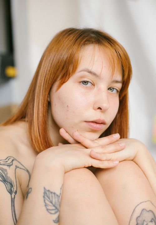 Free Close-up portrait of a young redhead woman with tattoos in a soft light setting. Stock Photo
