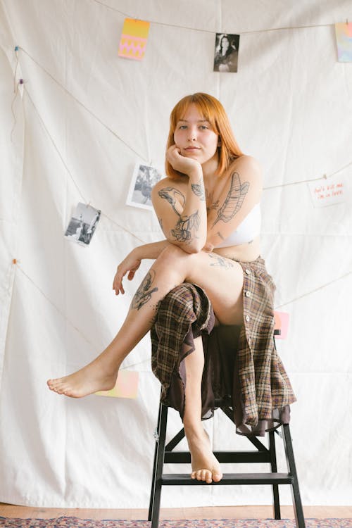 Free Tattooed Woman in White Bra and Plaid Shirt Sitting on High Chair with Crossed Legs Stock Photo