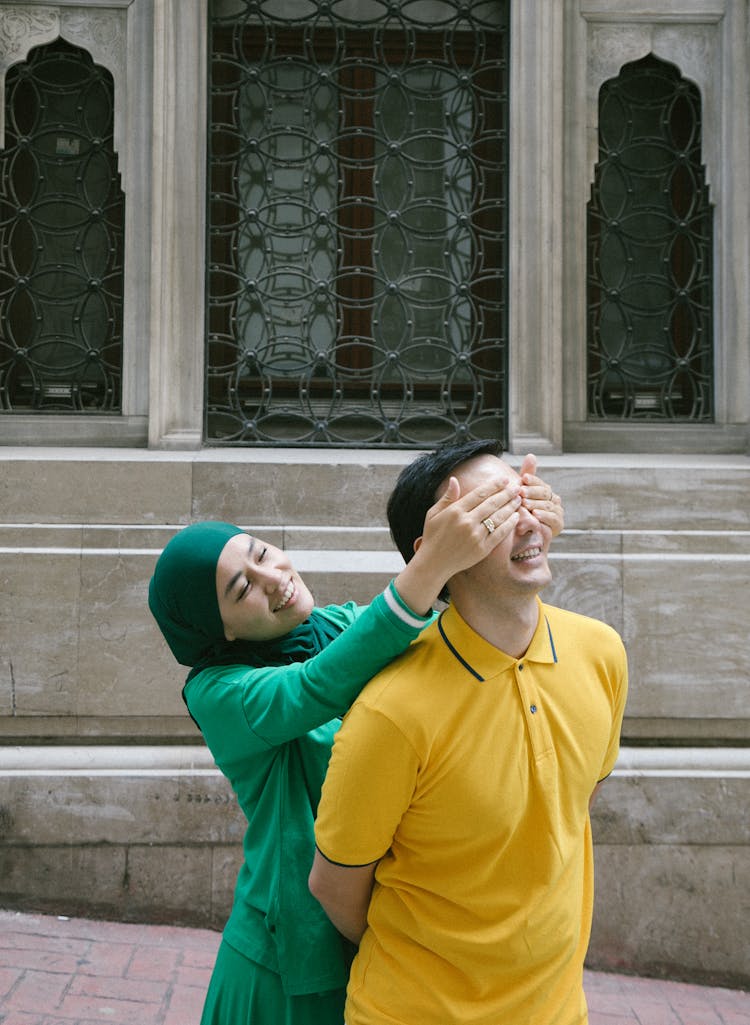 Woman In Green Hijab Closing Eyes Of Man In Yellow T-Shirt